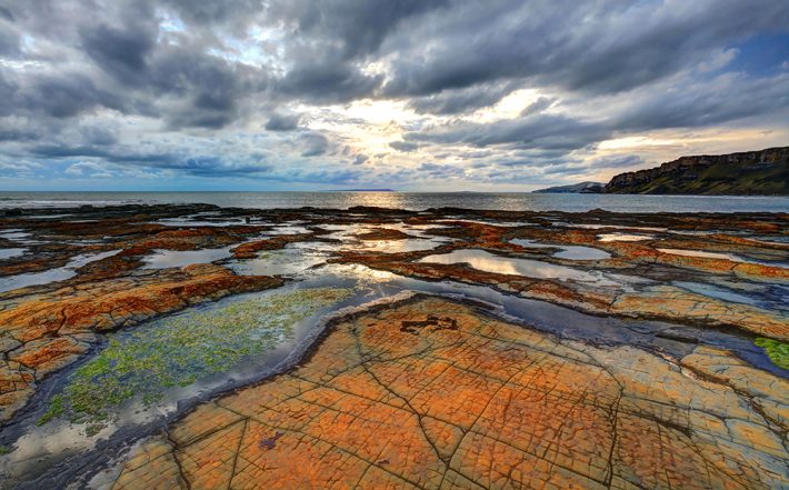 A view of puddles and rockpools on the edge of the sea with a dark and cloudy sky overhead