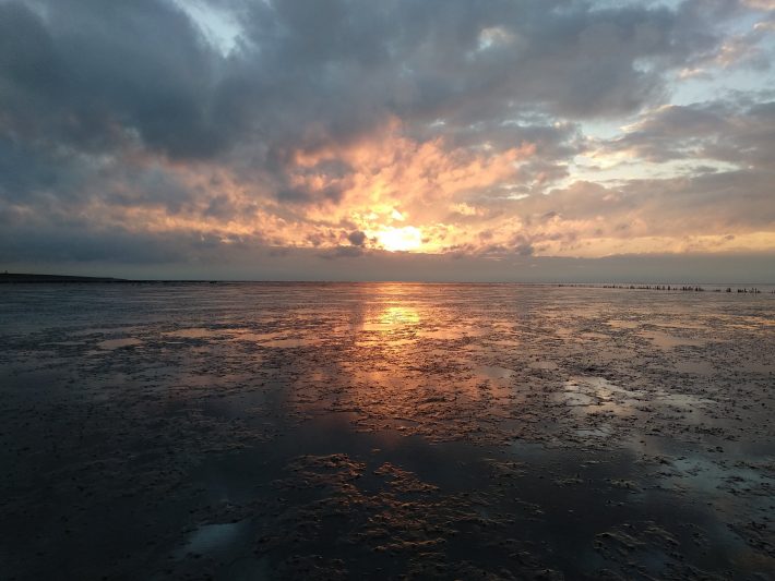 An orange sunset in a tidal flat overlooking a dike in The Netherlands