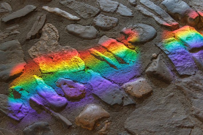 A rainbow casts a shadow over rocks, representing queer ecology