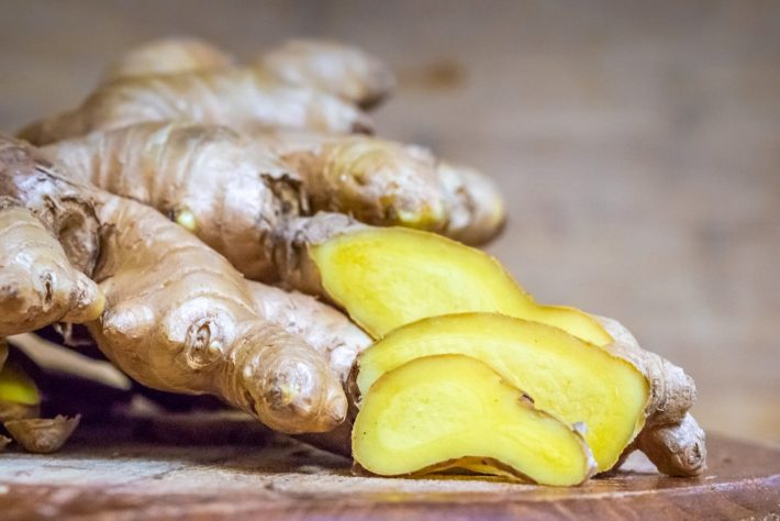 A ginger root on a wooden board, with a few slices cut to show the yellow insides - Ginger is one of the most common medicinal plants