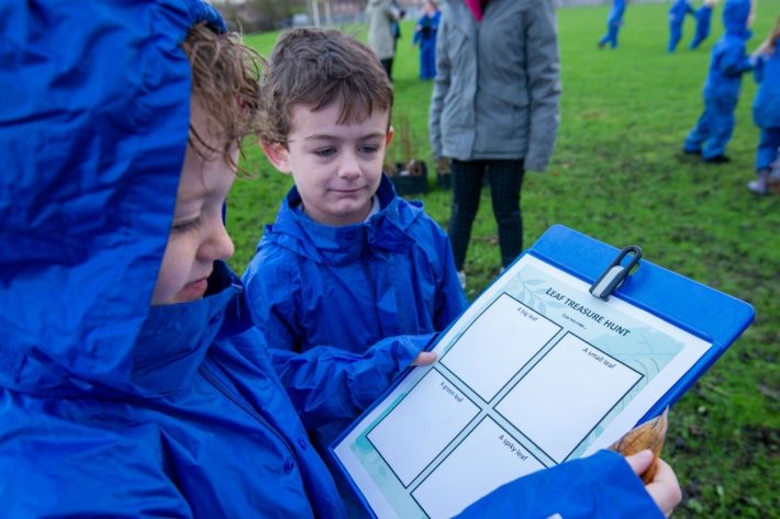 2 children on a school field, one holding a clipboard, engaging in the Connecting Schools to Nature programme